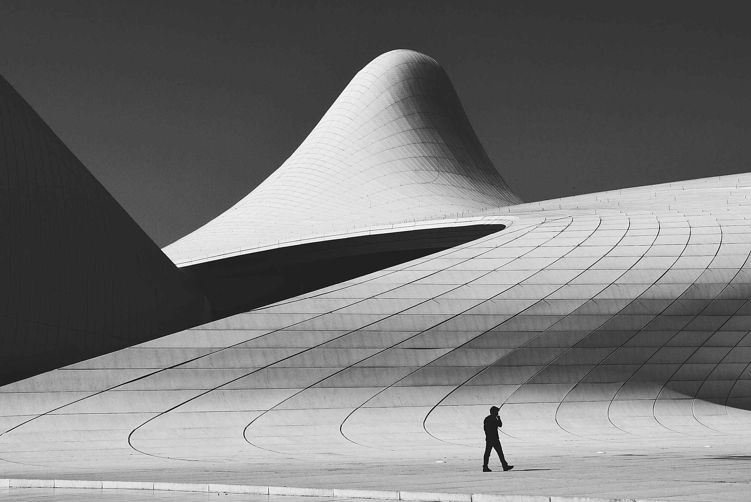 Monumental curved white architecture with a lone figure walking beneath it